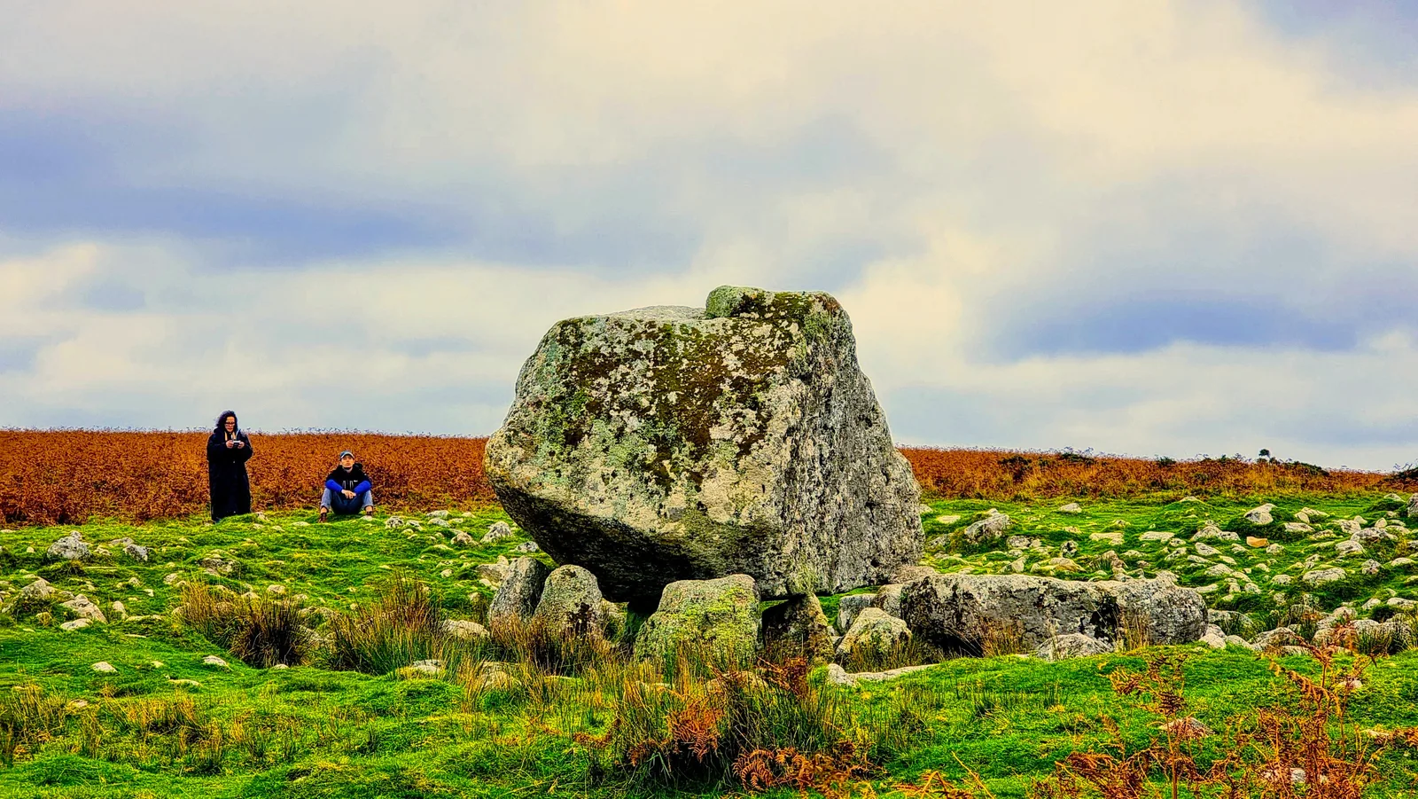 The capstone of Arthur’s Stone balanced on its supporting stones, with two figures in the distance