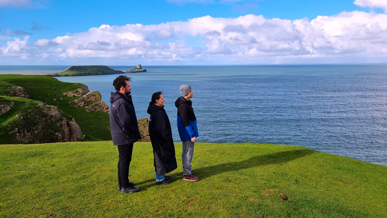 Three people looking out over the sea from the cliffs on the Gower Peninsula