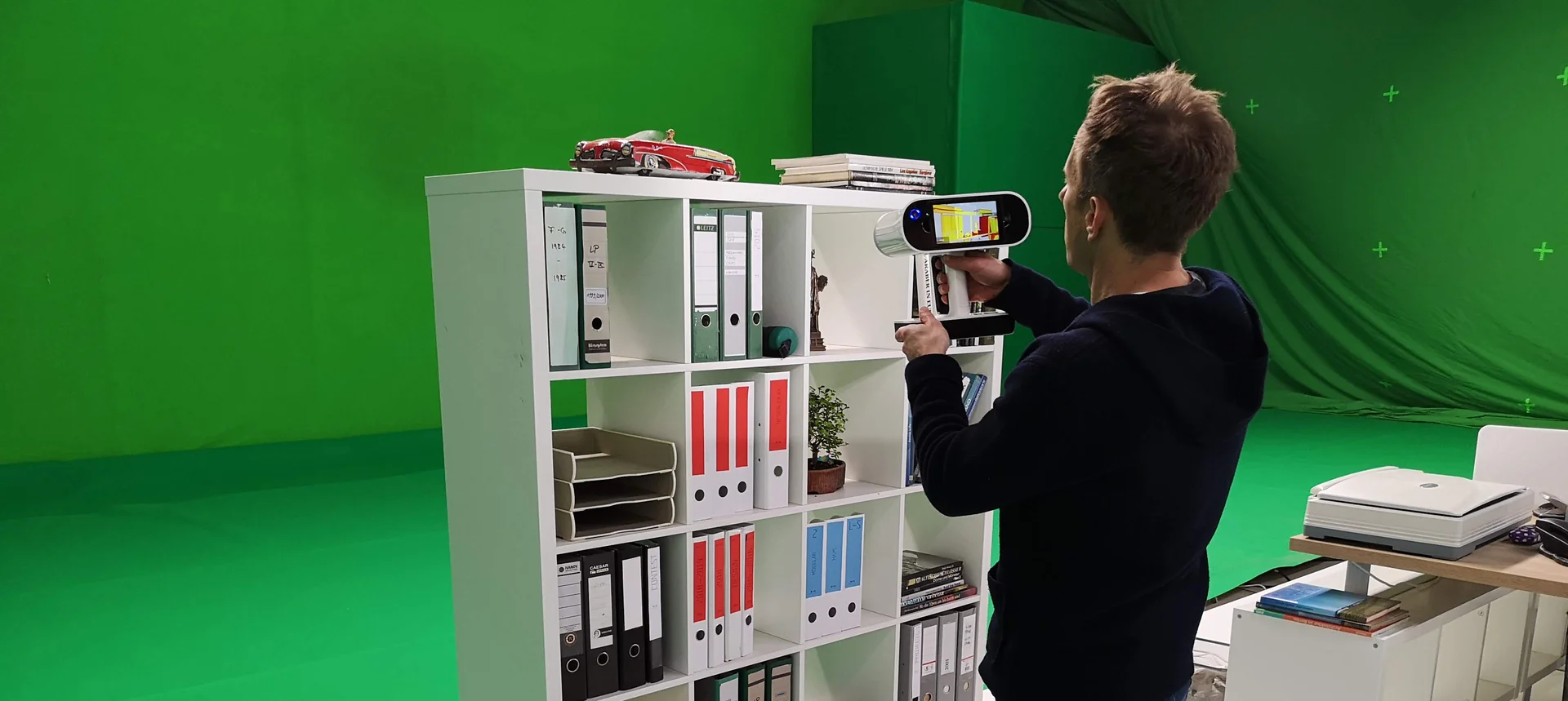Operator capturing a shelving unit with a handheld structured-light scanner on a green-screen stage