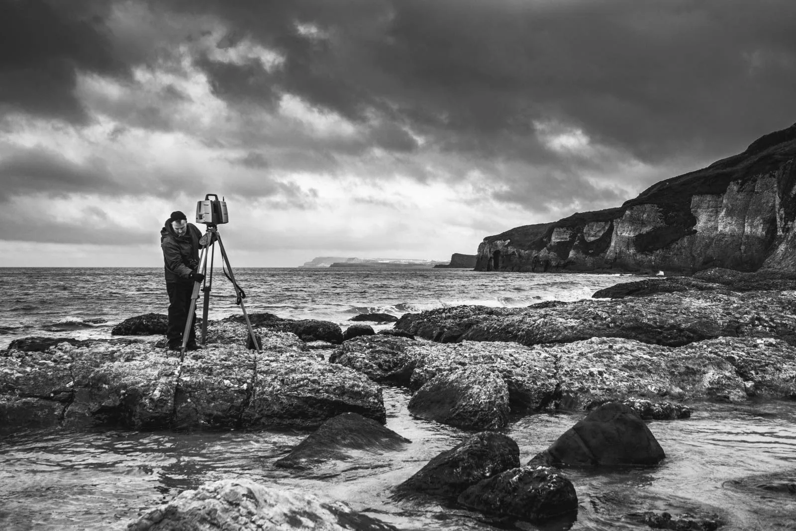 Surveyor operating LiDAR scanner on a dramatic rocky coastline