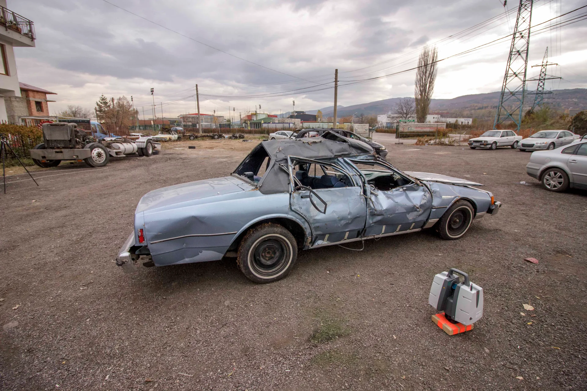 Wrecked Chevrolet sedan, rear three-quarter view with Leica scanner case in shot