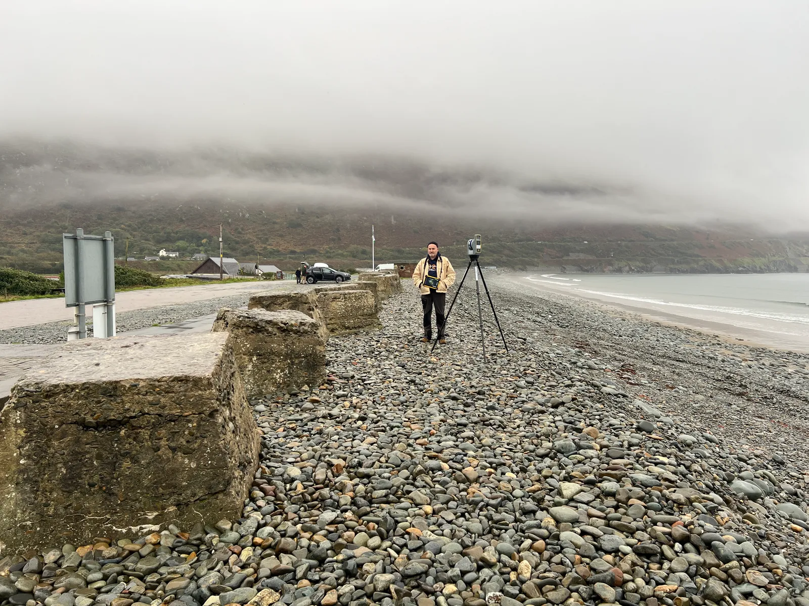 Kittiwake Digital operator with a tripod-mounted laser scanner on a pebble beach in misty North Wales